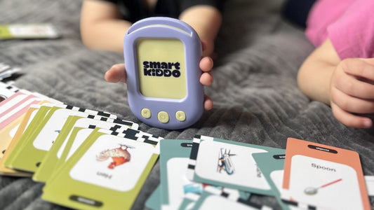 A child holding the SmartKiddo Pocket Vocab learning toy, surrounded by flashcards, illustrating the role of speech development in shaping a child's future